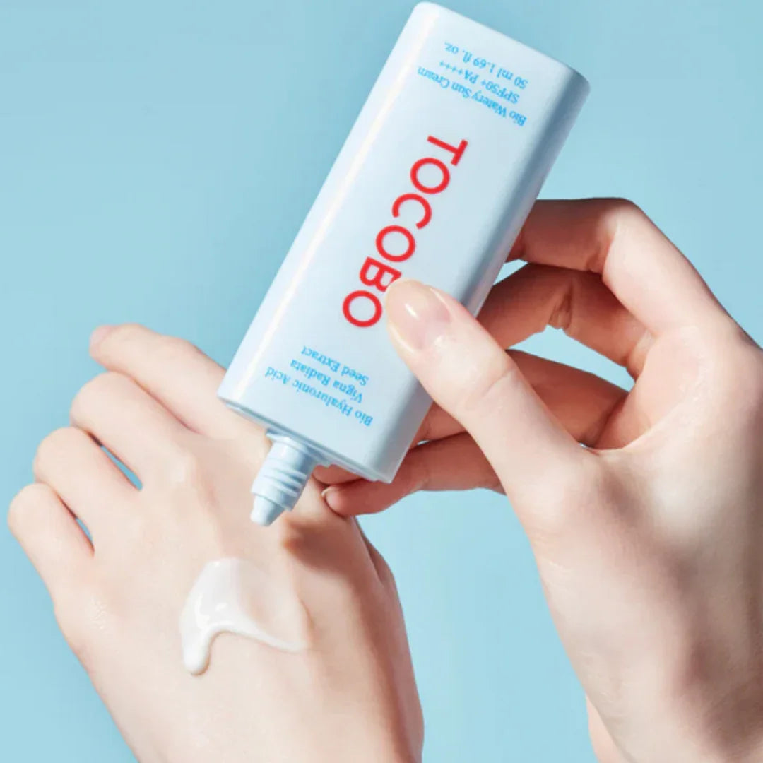 Person applying TOCOBO Bio Watery Sun Cream SPF50 PA+++ on hand against light blue background