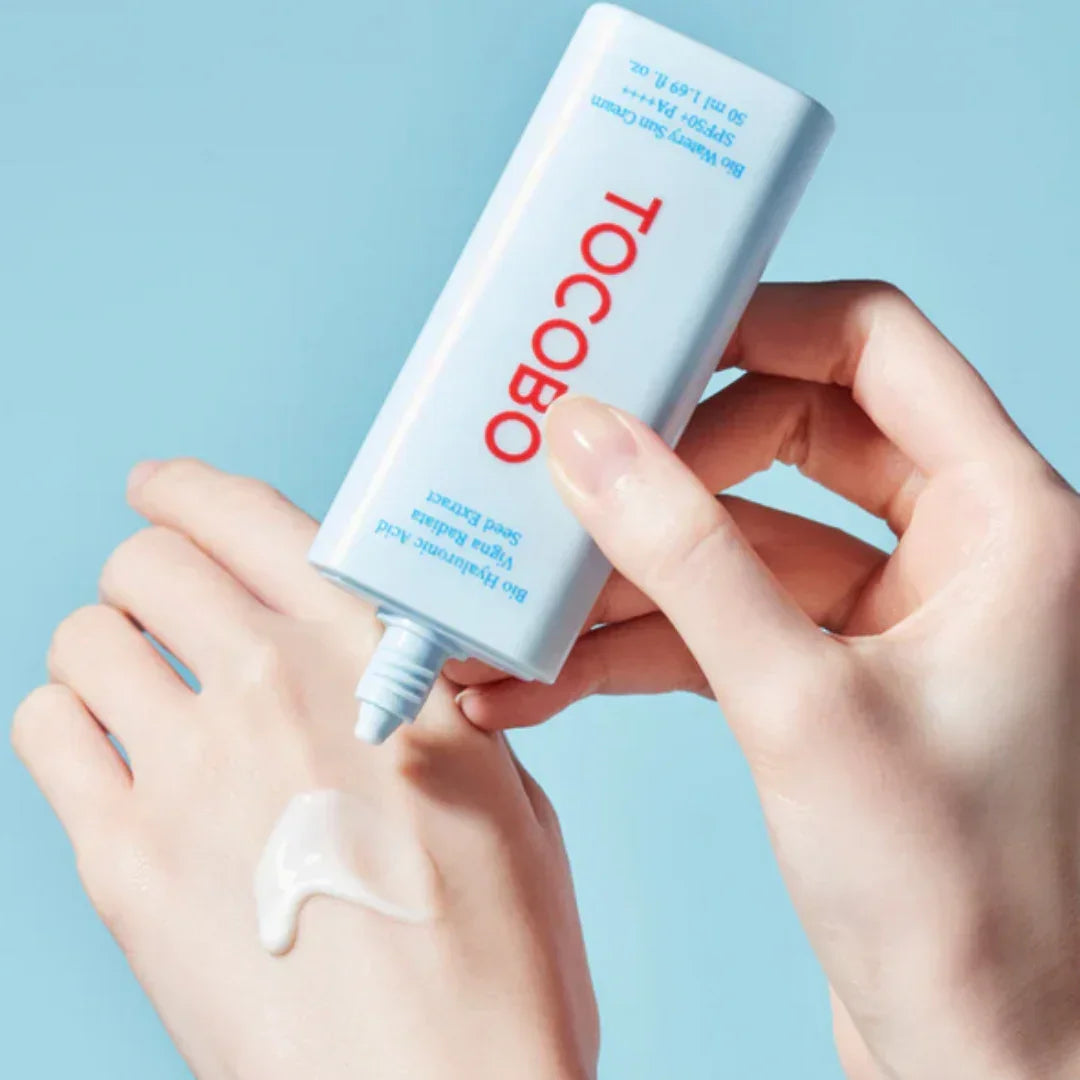Person applying TOCOBO Bio Watery Sun Cream SPF50 PA+++ on hand against light blue background