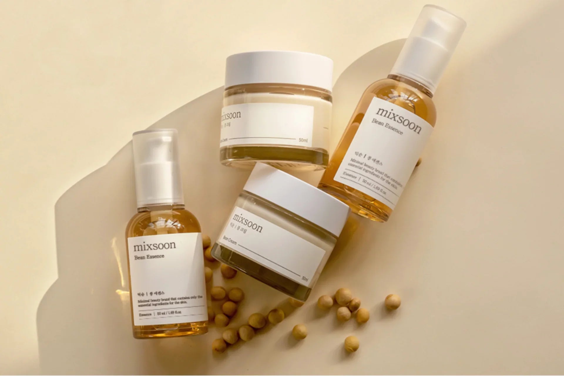 Mixsoon Korean skincare products including Bean Essence serum and Bean Cream jars with scattered mung beans on beige surface